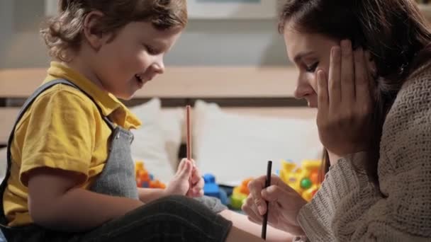 A mãe e a criança estão a desenhar. Bebê e sua mãe estão sentados na cama e desenhando alegremente. Movimento lento e close-up — Vídeo de Stock