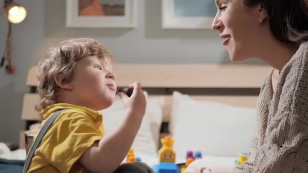 Maman embrasse bébé. Mère et enfant jouent le soir alors qu'ils sont assis sur le lit et la femme embrasse son bébé. Gros plan et ralenti — Video