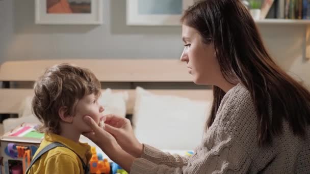 Maman essuie le visage de bébé. Mère et bébé s'assoient sur le lit dans la chambre et la femme essuie soigneusement le visage du garçon avec un chiffon humide. Gros plan et ralenti — Video