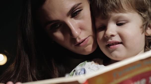 Мама и ребенок читают книгу. Крупный план лица мамы и ребенка, которые смотрят на книгу, читают перед сном. Вид спереди и замедленное движение — стоковое видео