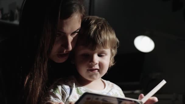Η μαμά διαβάζει βιβλία στο μωρό. Μητέρα και παιδί τη νύχτα στην κρεβατοκάμαρα και διαβάζοντας το βιβλίο πριν από το κρεβάτι. Κοντινό πλάνο και αργή κίνηση — Αρχείο Βίντεο