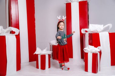 Mutlu, Noel kostümlü, arka planında büyük kırmızı hediyeler olan komik kız çocuğu..