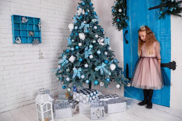 一个穿着连衣裙的可爱小女孩正在准备迎接新年 装饰圣诞树和检查礼物 — 图库照片