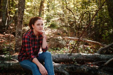 Sonbahar ormanlarında damalı gömlek ve kot pantolonlu gezgin hippi kadın. Soğuk hava, sonbahar renkleri. Seyahat tutkusu konsepti.