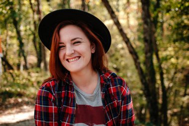 Sonbahar ormanlarında siyah şapkalı ve kareli gömlekli gezgin hippi kadın. Soğuk hava, sonbahar renkleri. Seyahat tutkusu konsepti.