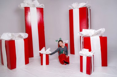 Mutlu, Noel kostümlü, arka planında büyük kırmızı hediyeler olan komik kız çocuğu..