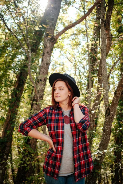 秋天的树林里 穿着黑色帽子和格子衬衫的旅行嬉皮士女人独自站在那里 寒冷的天气 秋天的颜色 流浪欲望概念 — 图库照片