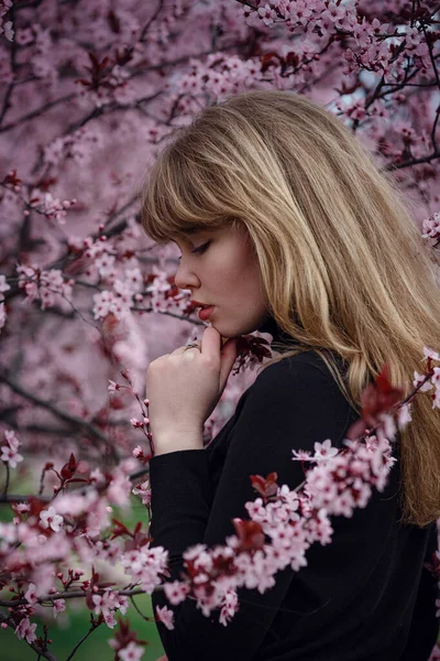 Outdoor fashion photo of a beautiful young lady in a pink cherry blossom garden. like a sakura in Japan.