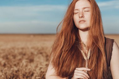 Buğday tarlasındaki genç kızıl kadın rahat görünüyor. Gün batımında tarımda bir kadın. Hasat ve Yaz Bayramı Festivali