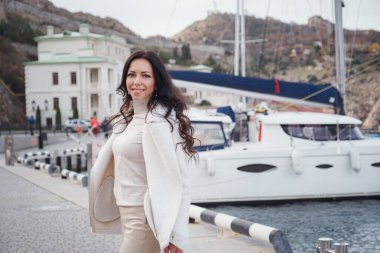 Kaygısız, bej elbiseli, sıcak ve rüzgarlı bir günde deniz manzarasının tadını çıkaran beyaz bir kadın. Deniz kenarına seyahat, seyahat, tatil konsepti