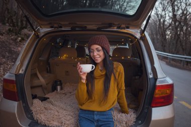 Arabanın bagajında oturan kadın. Gitmeye hazırlanıyorum. Arabasının bagajında oturan gülen genç bir kadın. Sonbahar araba gezisi. Hippi kurbağa seyahati, Sonbahar Kaçışı