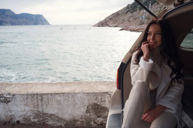 Bir arabanın bagajında dinlenen ve denize bakan bir kadın. Günbatımında sonbahar gezisi. Hareket özgürlüğü kavramı. Sonbahar hafta sonu. Tek başına mı seyahat edersin yoksa tek başına mı?.