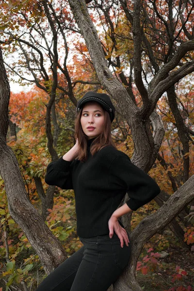 Cute asian woman in a good mood poses in autumn day, enjoying the good weather. The art of the work of a romantic woman. Pretty soft model looks at the camera.