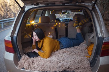 Genç güzel esmer, arabasının bagajında dinlenmekten hoşlanıyor. Sarı bir çelenk ve bej bir ekose rahat bir ortam, e-posta okuyan bir kadın, habercilerle sohbet eden ve bilgisayardaki video konferansında konuşan bir kadın.