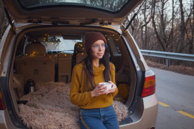 Arabanın bagajında oturan kadın. Gitmeye hazırlanıyorum. Arabasının bagajında oturan gülen genç bir kadın. Sonbahar araba gezisi. Hippi kurbağa seyahati, Sonbahar Kaçışı