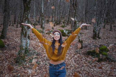 pozitif neşeli kadın sonbaharı parkta ya da ormanda geçirir sarı kazak, şapka ve gözlük takar. Sonbahar ormanı yolculuğundaki neşeli hippi kız.