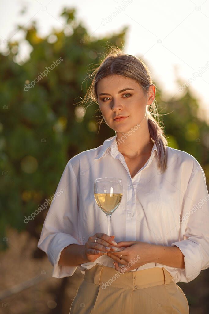 Vintner woman tasting white wine from a glass in a vineyard. vineyards background at sunset.