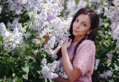 Bahar bahçesinde yürüyen ve leylak kokusunun tadını çıkaran güzel bir genç kadın. Aromaterapi ve Bahar Konsepti