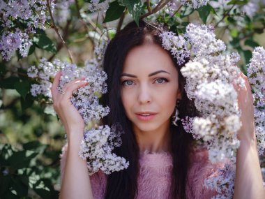 Bahar bahçesinde yürüyen ve leylak kokusunun tadını çıkaran güzel bir genç kadın. Aromaterapi ve Bahar Konsepti