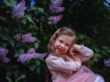 Pembe şık elbiseli güzel bir kız leylak bahçesinde yürüyor. Şefkat ve çocukluk fikri ve konsepti