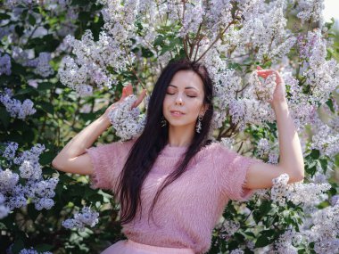Bahar bahçesinde yürüyen ve leylak kokusunun tadını çıkaran güzel bir genç kadın. Aromaterapi ve Bahar Konsepti