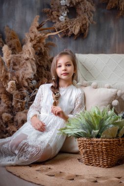 Evde güzel elbiseli şirin küçük bir kız. Uzun dalgalı saçlı, çiçekli retro pastel elbiseli prenses. Güzel bir boho odasında küçük bir bayan