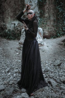 Siyah uzun elbiseli gizemli kel kadın. Tapınağın yakınındaki gotik pagan kadın ve putlar. Vampir karanlık, gizemli bir ormanda yürüyor..