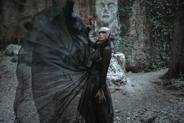 穿着黑色长裙的神秘鬼秃头女人 哥特式异教徒女士靠近寺庙和偶像 吸血鬼在一片漆黑的神秘森林中行走 — 图库照片
