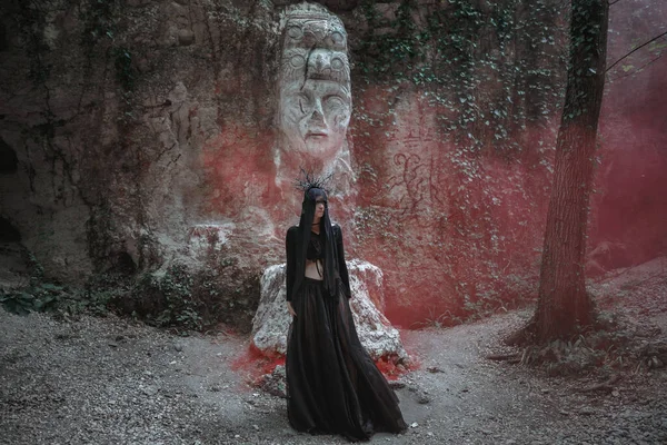 身披黑衣 头戴皇冠的年轻女巫站在漆黑多雾的森林里 深色派对服装之间的光晕 — 图库照片