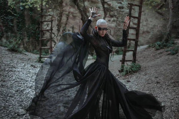 穿着黑色长裙的神秘鬼秃头女人 哥特式异教徒女士靠近寺庙和偶像 吸血鬼在一片漆黑的神秘森林中行走 — 图库照片