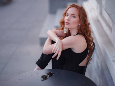 Siyah takım elbiseli kızıl, genç bir kadın bahar kasabasında yürüyor. Avrupa 'da sokak kafesinde poz veriyor