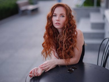 Siyah takım elbiseli kızıl, genç bir kadın bahar kasabasında yürüyor. Avrupa 'da sokak kafesinde poz veriyor