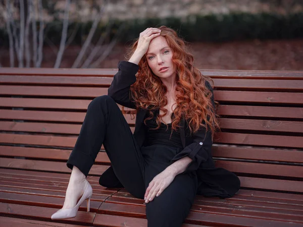 Kızıl genç kadın bahar şehrinde yürüyor. İş kadını bankta oturuyor.