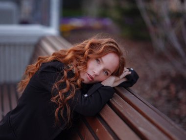 Kızıl genç kadın bahar şehrinde yürüyor. İş kadını bankta oturuyor.