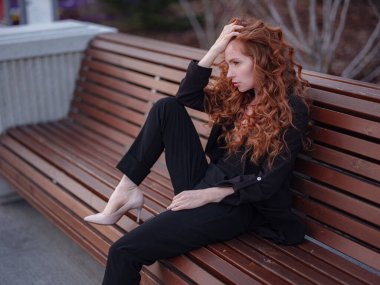 Kızıl genç kadın bahar şehrinde yürüyor. İş kadını bankta oturuyor.