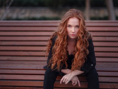 Kızıl genç kadın bahar şehrinde yürüyor. İş kadını bankta oturuyor.