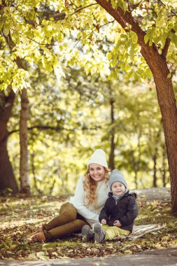 Anne ve oğlu güneşli bir sonbahar gününde dışarıda yürüyorlar. Sonbahar tarzı giyinmiş bir aile. Birlikte mutluyuz.