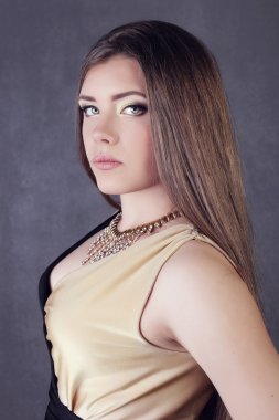 Young brunette lady in black ang golden dress posing on grey background