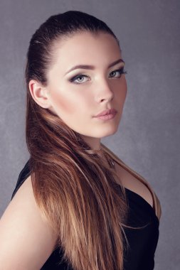 Young brunette lady in black ang golden dress posing on grey background