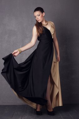 Young brunette lady in black ang golden dress posing on grey background