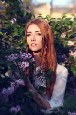 Redhead girl near lilac tree in the garden. sunset
