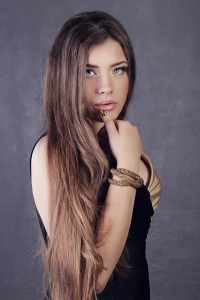 Young brunette lady in black ang golden dress posing on grey background — Stok fotoğraf