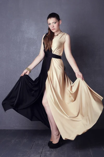 Young brunette lady in black ang golden dress posing on grey background — Stok fotoğraf