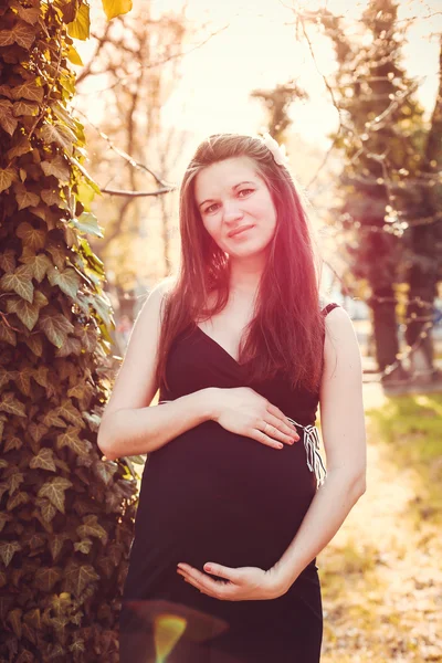 Pregnant woman stands next to the sunset in the garden — Stock Photo, Image