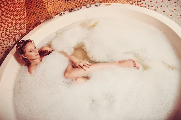 Mujer joven con el pelo rojo tomar baño de burbujas con vela . — Foto de Stock