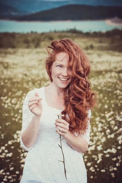 Bilden av vacker kvinna liggande på kamomill fält, glad kvinna håller i hand vacker vit blomma, glad tjej vilar på daisy äng, avkoppling utomhus på våren semester koncept — Stockfoto