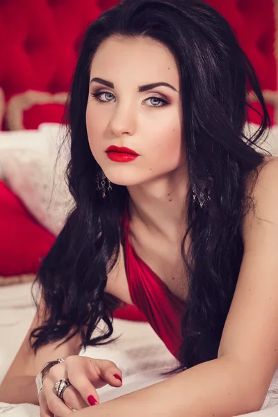 エレガントな赤で黒い髪とセクシーなグラマー女性のドレスの豪華なベッドルーム — ストック写真