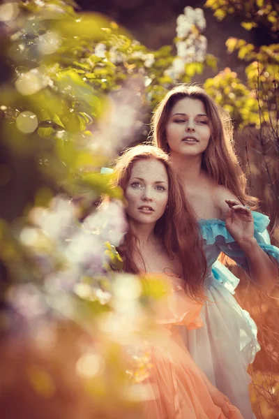 Hermosas mujeres disfrutando de jardín lila, mujeres jóvenes con flores — Foto de Stock