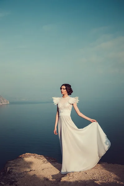 Beautiful bride posing on the coast with angelic dress — Stock Photo, Image