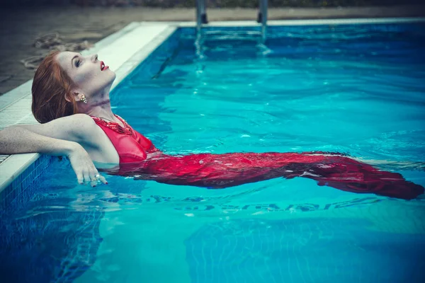 Junge sexy Frau, die im roten Kleid auf dem Swimmingpool schwimmt. Schönheitsschuss — Stockfoto